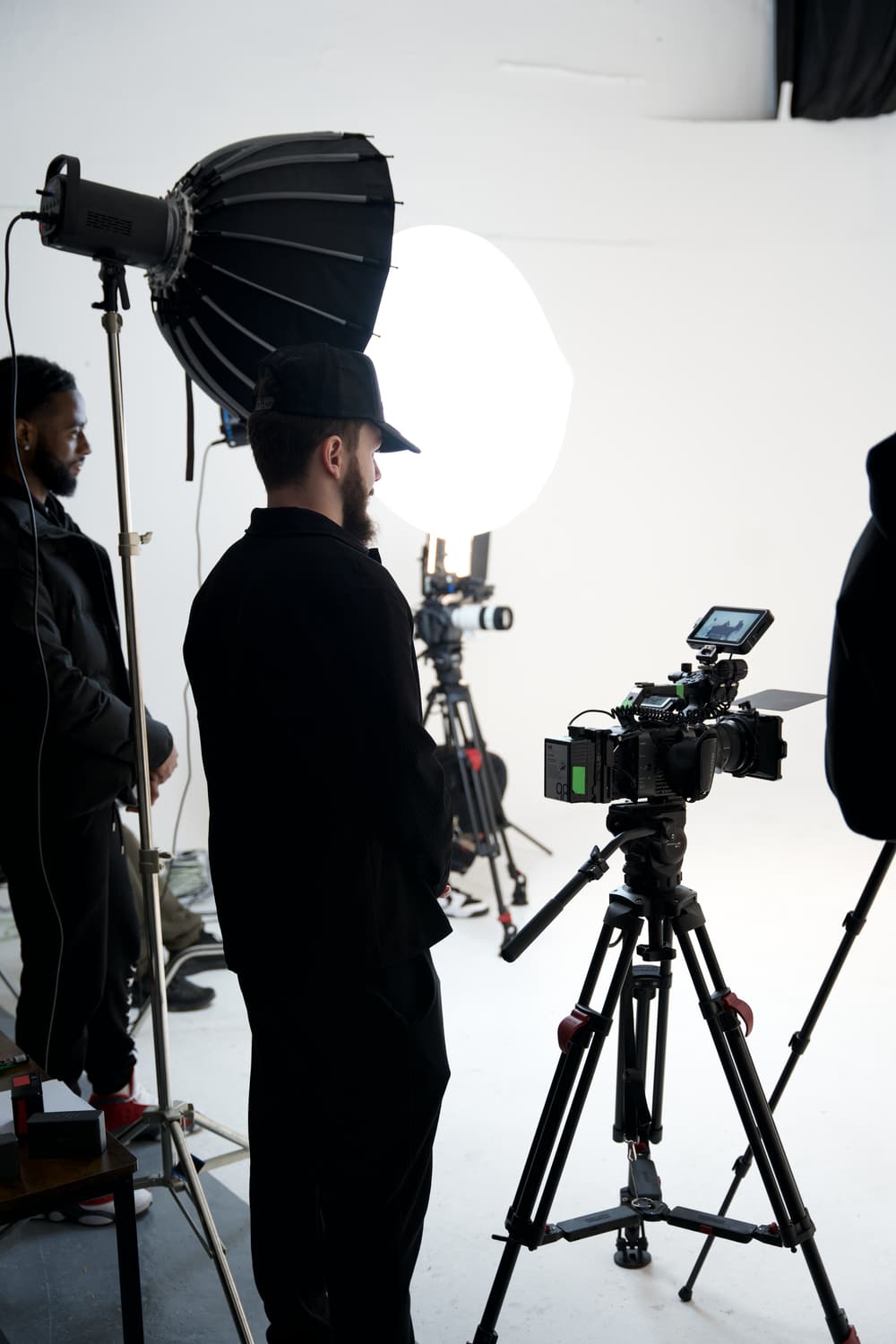 The crew on a lit studio set, two cameras on tripods behind a softbox